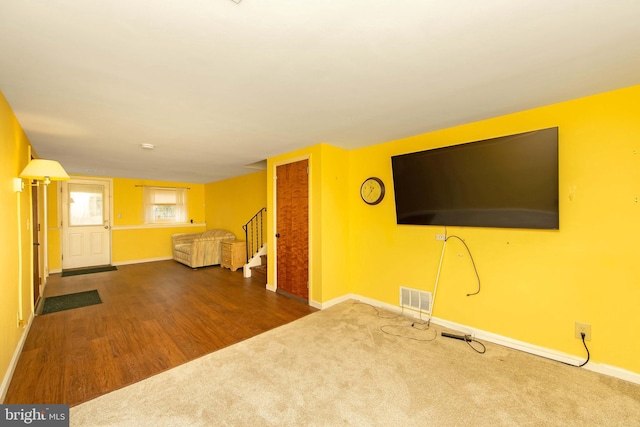 unfurnished living room with carpet floors, visible vents, stairway, wood finished floors, and baseboards