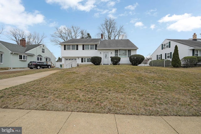 tri-level home with driveway, a garage, a chimney, and a front yard