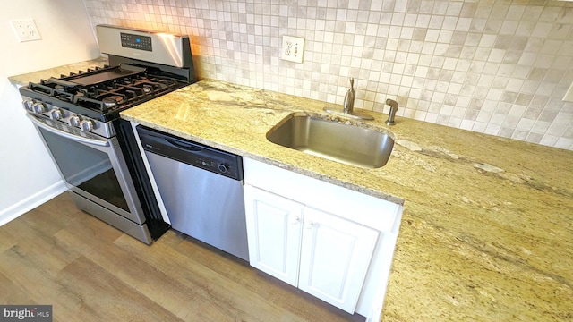 kitchen with white cabinets, decorative backsplash, appliances with stainless steel finishes, wood finished floors, and a sink