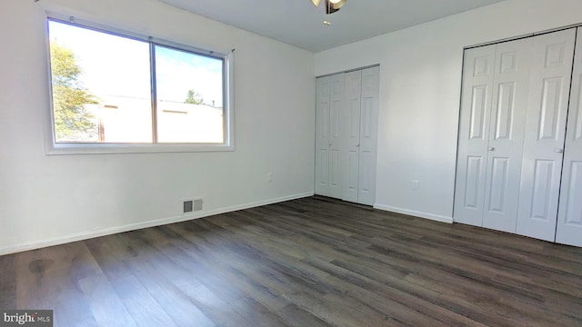 unfurnished bedroom featuring dark wood-style flooring, visible vents, baseboards, and two closets