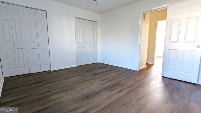 unfurnished bedroom featuring dark wood-style floors, baseboards, and two closets