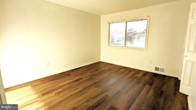 spare room featuring dark wood-type flooring, visible vents, and baseboards