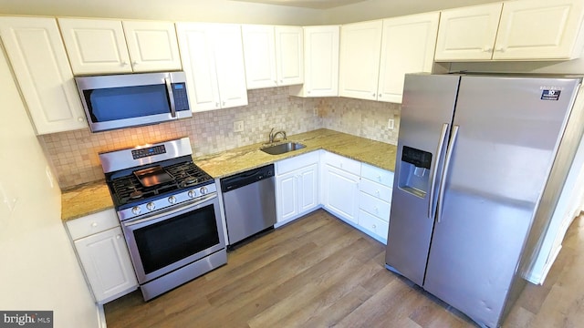 kitchen with wood finished floors, light stone countertops, stainless steel appliances, white cabinetry, and a sink