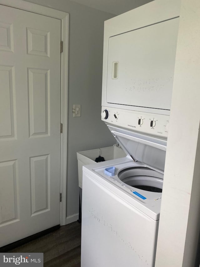 laundry area featuring stacked washer / drying machine, laundry area, and dark wood-style flooring