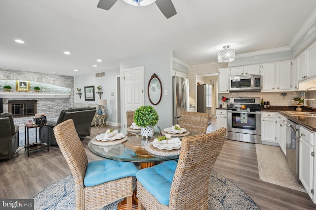 dining space with light wood finished floors, a stone fireplace, recessed lighting, and crown molding