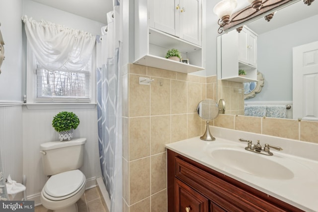 bathroom featuring a wainscoted wall, tile walls, toilet, vanity, and tile patterned flooring