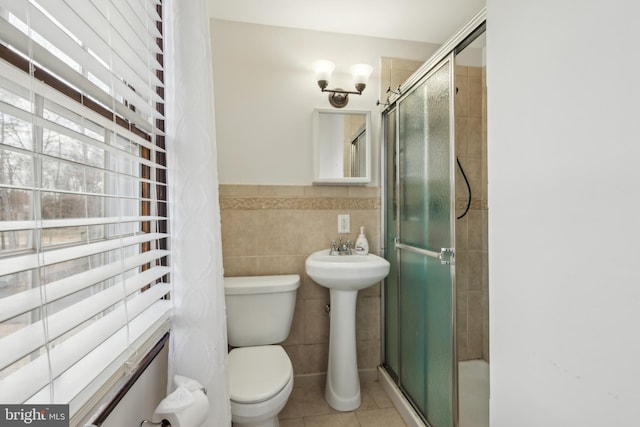 bathroom with toilet, a stall shower, tile patterned flooring, and tile walls