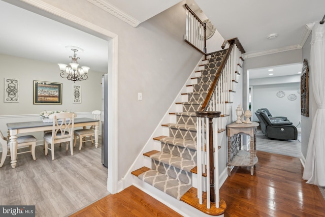 stairs featuring baseboards, a notable chandelier, wood finished floors, and crown molding