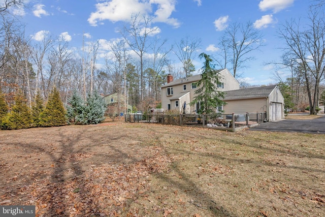 back of house with aphalt driveway, an attached garage, an outdoor structure, fence, and a chimney