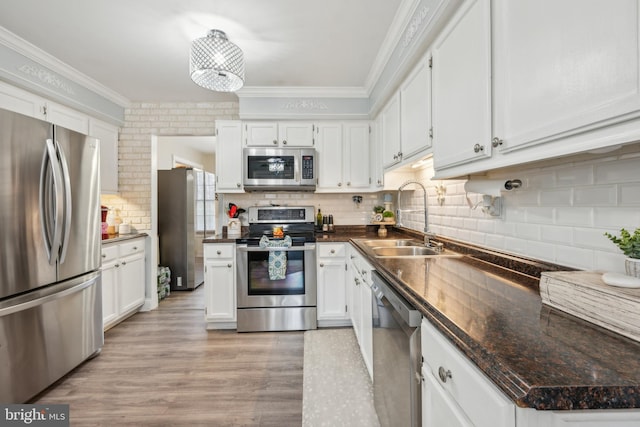 kitchen with dark countertops, ornamental molding, stainless steel appliances, light wood-style floors, and a sink