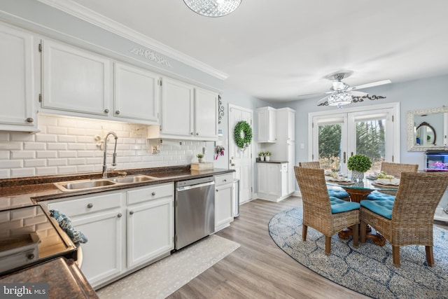 kitchen featuring dark countertops, decorative backsplash, white cabinets, a sink, and dishwasher