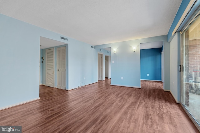 unfurnished room with baseboards, a textured ceiling, visible vents, and wood finished floors