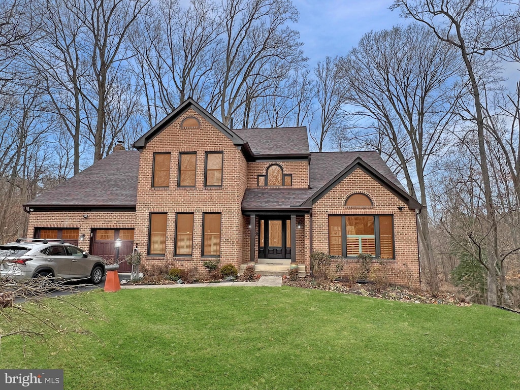 traditional-style house with driveway, roof with shingles, an attached garage, a front lawn, and brick siding