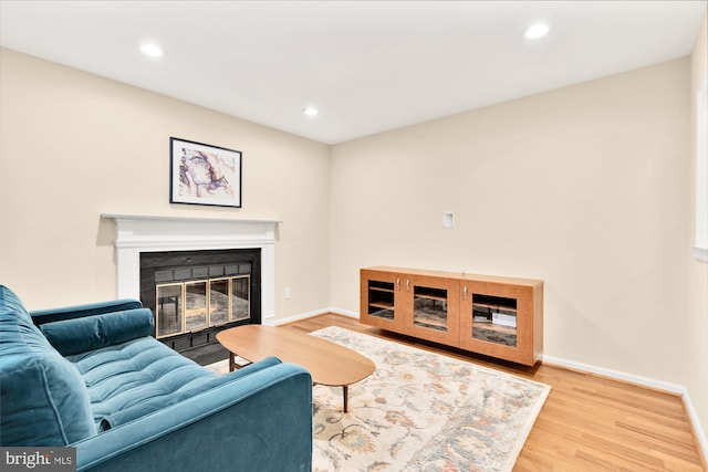 living room featuring a glass covered fireplace, recessed lighting, baseboards, and wood finished floors