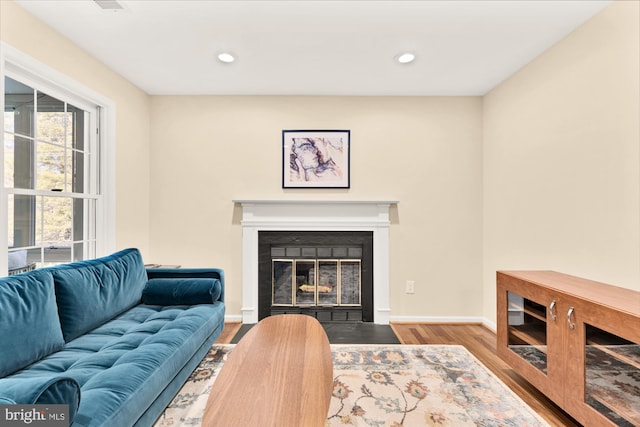 living room with recessed lighting, wood finished floors, baseboards, and a fireplace with flush hearth