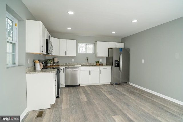 kitchen with baseboards, visible vents, stainless steel appliances, light wood-style floors, and a sink