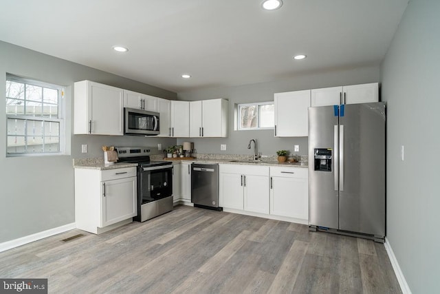 kitchen with stainless steel appliances, light wood-style floors, white cabinetry, and a sink