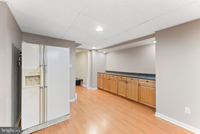 interior space featuring baseboards, a drop ceiling, dark countertops, light wood-type flooring, and white fridge with ice dispenser