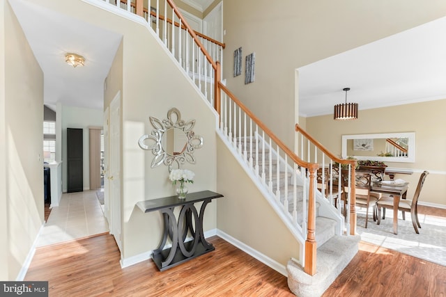 stairs featuring ornamental molding, wood finished floors, a towering ceiling, and baseboards