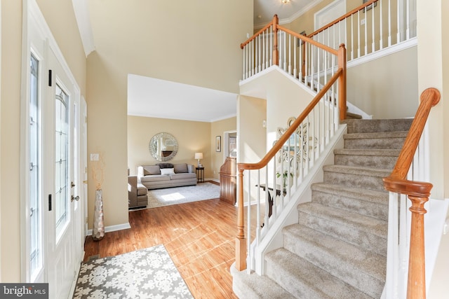 entryway featuring ornamental molding, a high ceiling, wood finished floors, and baseboards