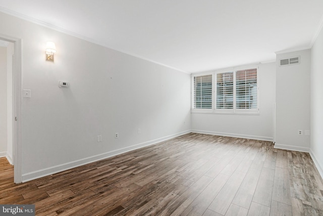 spare room with baseboards, visible vents, wood finished floors, and ornamental molding