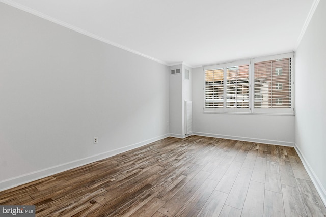 spare room featuring baseboards, crown molding, visible vents, and wood finished floors