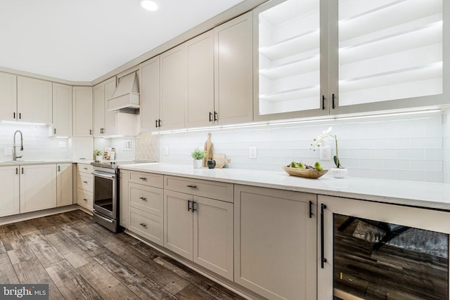 kitchen featuring dark wood-style flooring, stainless steel electric range oven, custom exhaust hood, decorative backsplash, and beverage cooler