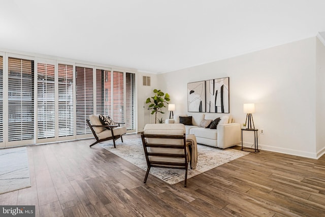 living area with ornamental molding, wood finished floors, visible vents, and baseboards