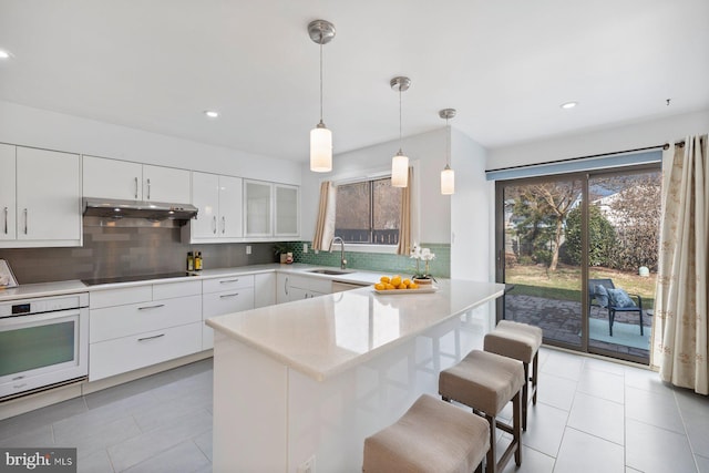 kitchen featuring a peninsula, a sink, under cabinet range hood, white oven, and black electric stovetop