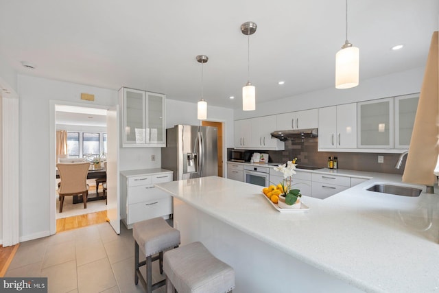 kitchen with black appliances, a sink, under cabinet range hood, backsplash, and a peninsula