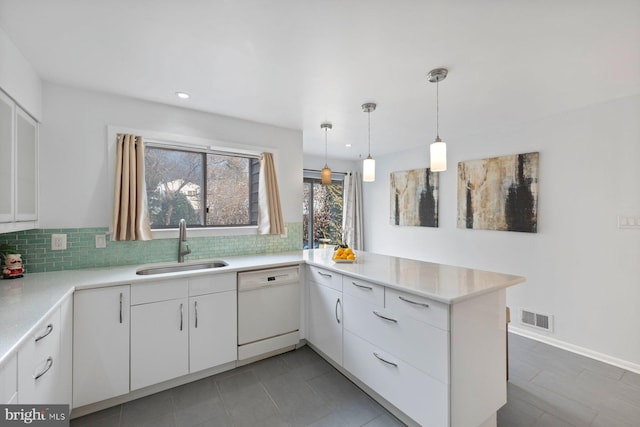 kitchen featuring visible vents, white dishwasher, a sink, white cabinets, and tasteful backsplash