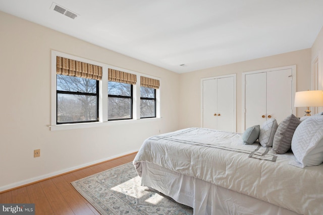 bedroom with wood-type flooring, baseboards, visible vents, and two closets