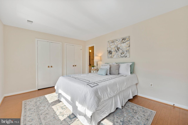 bedroom featuring baseboards, multiple closets, and hardwood / wood-style floors