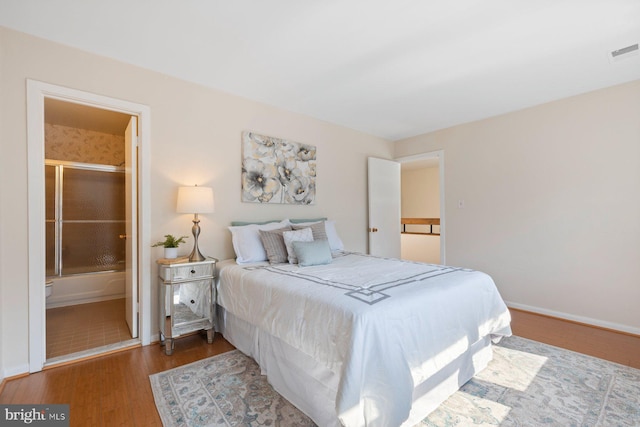 bedroom featuring connected bathroom, visible vents, baseboards, and wood finished floors