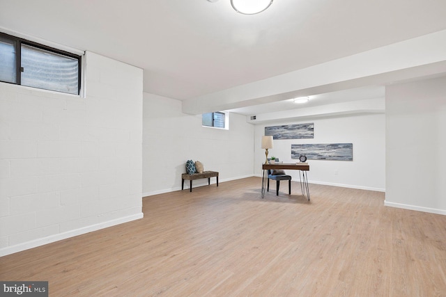 below grade area with light wood finished floors, concrete block wall, and baseboards