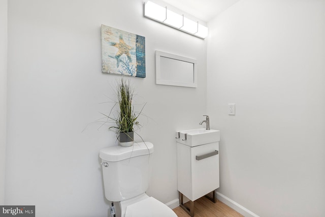 bathroom featuring wood finished floors, toilet, baseboards, and a sink