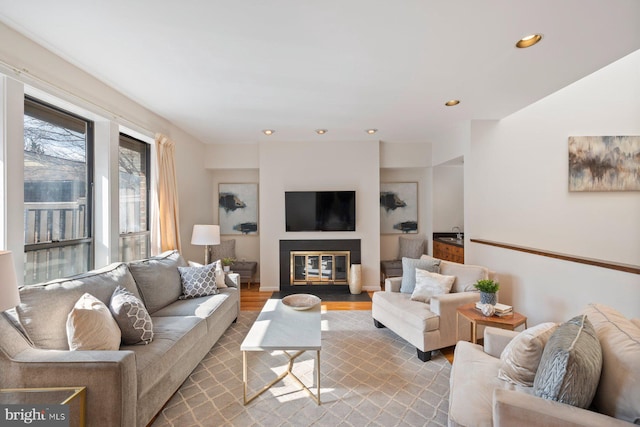 living area with recessed lighting, a fireplace with flush hearth, and wood finished floors