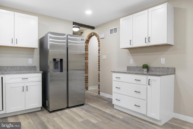 kitchen featuring stainless steel fridge with ice dispenser, visible vents, white cabinets, light wood-type flooring, and baseboards