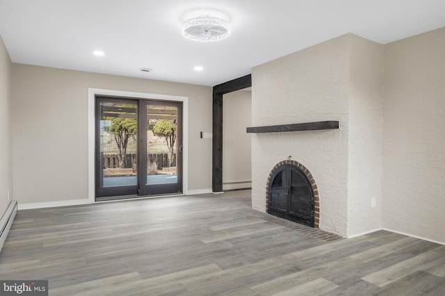 unfurnished living room featuring baseboards, wood finished floors, a brick fireplace, a baseboard heating unit, and recessed lighting