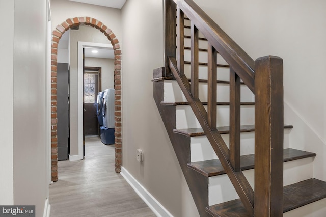 stairs featuring arched walkways, baseboards, and wood finished floors