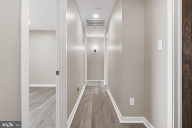 hallway featuring baseboards, attic access, visible vents, and wood finished floors