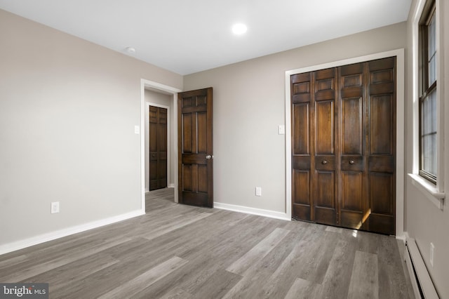 unfurnished bedroom with light wood finished floors, a closet, a baseboard radiator, and baseboards