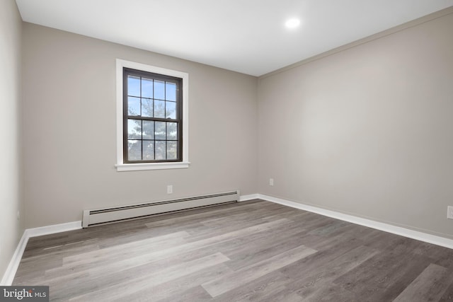 unfurnished room featuring a baseboard radiator, baseboards, and wood finished floors