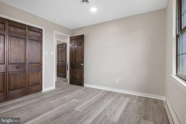 unfurnished bedroom with light wood-type flooring, a baseboard radiator, visible vents, and baseboards