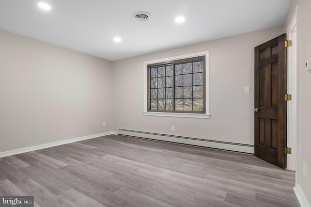 unfurnished room featuring a baseboard heating unit, visible vents, and wood finished floors