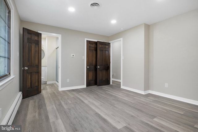 unfurnished bedroom with a baseboard heating unit, light wood-type flooring, visible vents, and baseboards