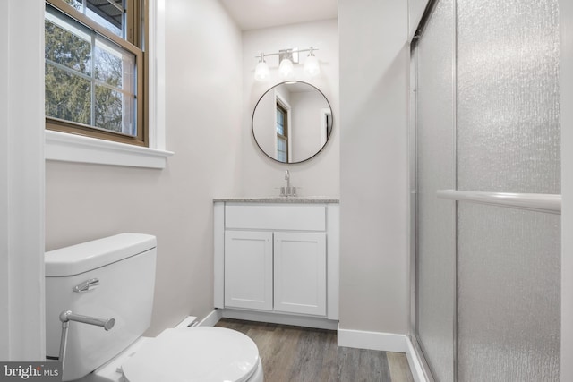 bathroom with toilet, wood finished floors, vanity, baseboards, and a shower with door