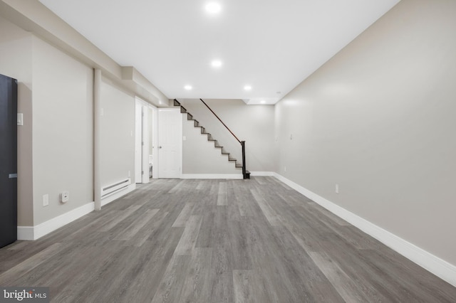 finished below grade area with baseboards, wood finished floors, stairs, baseboard heating, and recessed lighting