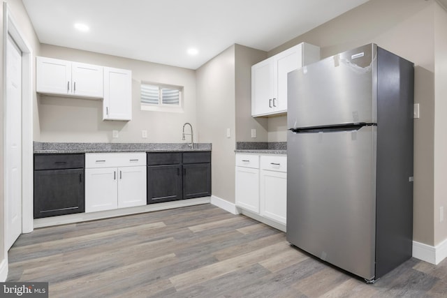 kitchen with stone countertops, freestanding refrigerator, white cabinets, and light wood-style flooring