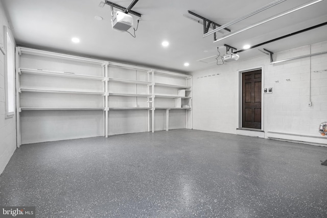 garage with a garage door opener, concrete block wall, and a baseboard heating unit